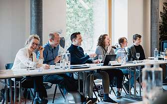 Sechs Personen lachen während einer Besprechung an einem Tisch.