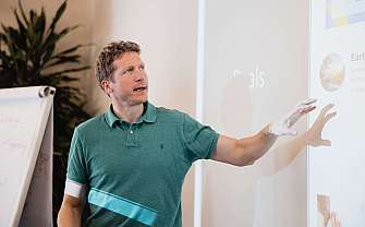 Mann zeigt auf eine Präsentationsfolie während einer Besprechung.