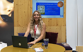 A woman is sitting at a table with a laptop and pens.